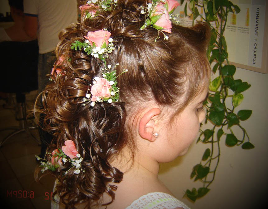 Penteado preso com cachos e tranças, decorado com rosas cor-de-rosa naturais entrelaçadas no cabelo.
