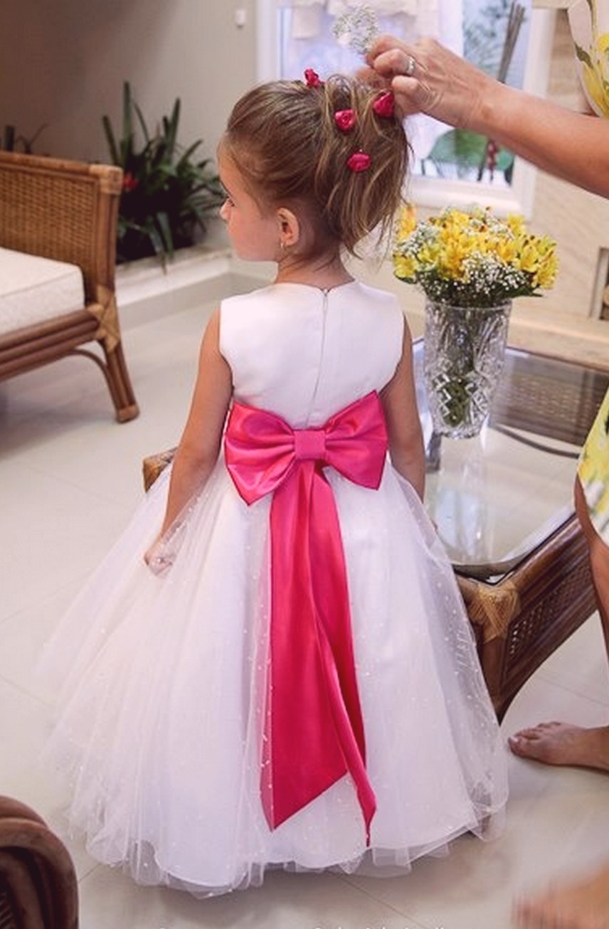 Daminha de costas com penteado de coque bagunçado e flores vermelhas e rosas presas no cabelo.