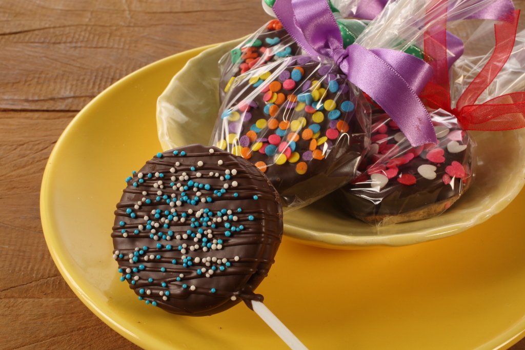 Biscoitos decorados em formato de macacão de bebê no palito